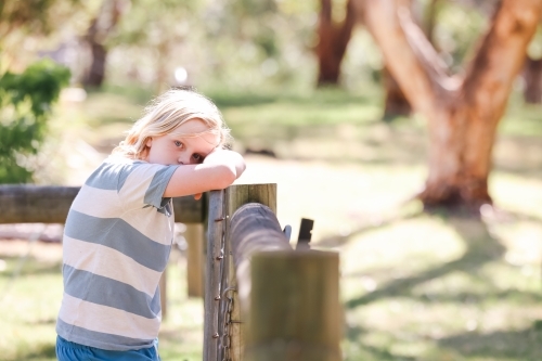 Blonde pre-teen boy leaning on fence with serious expression - Australian Stock Image