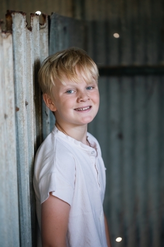 Blonde pre-teen boy with relaxed pose sitting in rustic outdoor county setting - Australian Stock Image