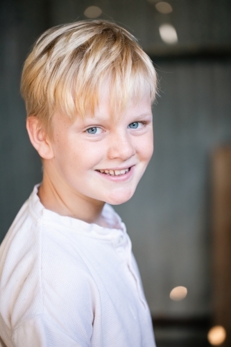Blonde pre-teen boy with relaxed pose sitting in rustic outdoor county setting - Australian Stock Image