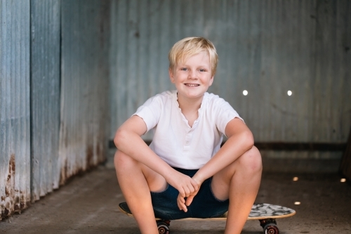 blonde pre-teen boy with relaxed pose sitting in rustic outdoor county setting - Australian Stock Image
