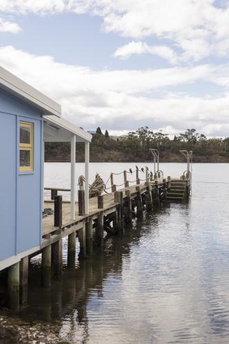Blue boat house with jetty over water at Cornelian Bay - Australian Stock Image