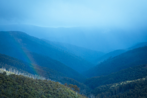 Blue hazy clouds and rainbow over mountain range at Mt Hotham - Australian Stock Image