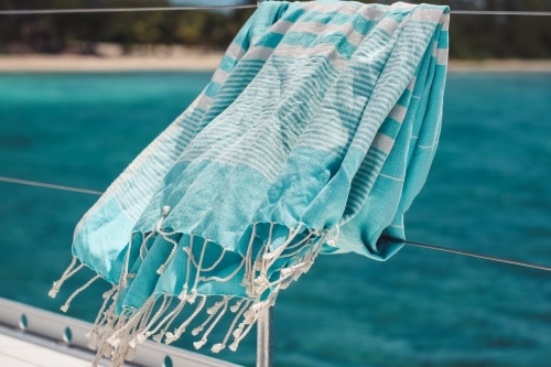 Blue turkish towel blowing on wire railing of boat on the water - Australian Stock Image