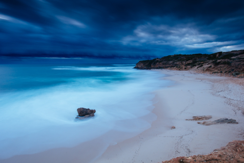 blue water and dark cloud on Number Sixteen Beach with incoming storm at dusk in Rye, Victoria - Australian Stock Image