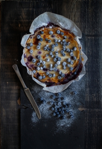 Blueberry cheesecake in baking paper on black background - Australian Stock Image