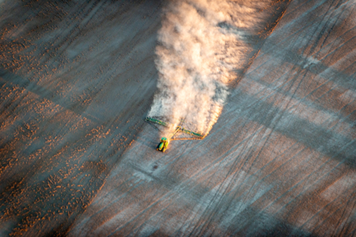 blurred tractor trailing dust across a dry paddock in early morning light, viewed from above - Australian Stock Image