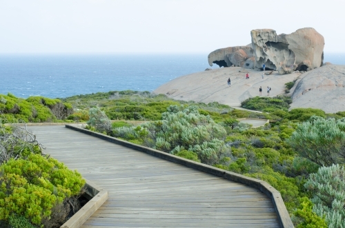 Boardwalk through brush to large rock formation by the ocean