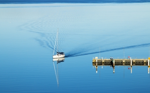 Boat coming into dock with ripples in wake - Australian Stock Image