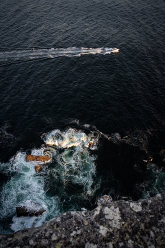 Boat passing a cliff and rocks in the sunset - Australian Stock Image
