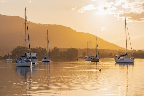 Boats and yachts moored on a still river in front of golden sunset - Australian Stock Image