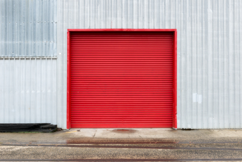 Bold red roller door on corrugated metal warehouse wall. - Australian Stock Image