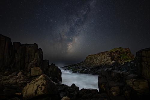 bombo milky way stars with coastal rocks and water in foreground - Australian Stock Image
