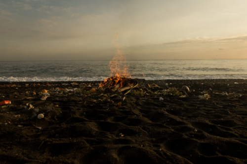 Bonfire burning on the dark sand at the beach at sunset - Australian Stock Image