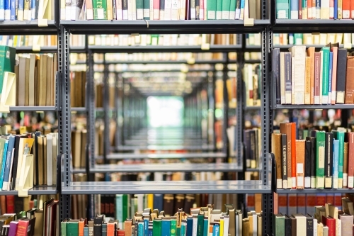 Books in rows on library shelves and window light through shelving - Australian Stock Image
