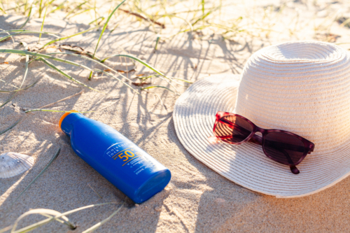 Bottle of 50+ SPF sunscreen on beach sand by sun hat and sunglasses  - Australian Stock Image
