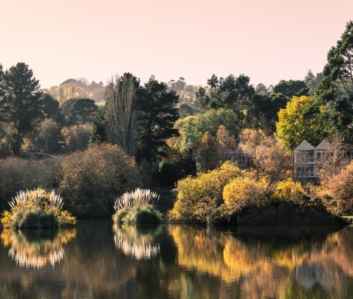 Boutique hotel by the lake, surrounded in lush green, yellow and brown trees, with water reflections - Australian Stock Image