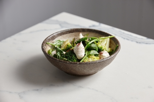 Bowl of greens, broccoli and burrata cheese on a table - Australian Stock Image