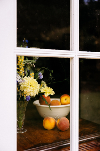 bowl of peaches and some flowers through a door - Australian Stock Image
