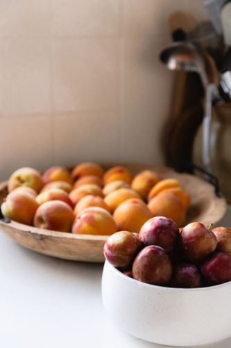 Bowls of freshly picked stone fruit on white kitchen bench - Australian Stock Image