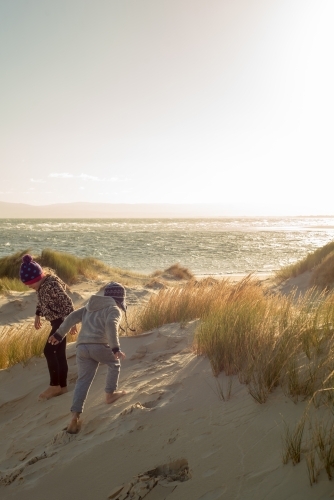 Boy and girl playing on sand dunes at sunset - Australian Stock Image