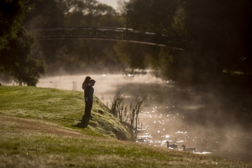 Boy and girl rugged up on cold morning fog day watching ducks in river