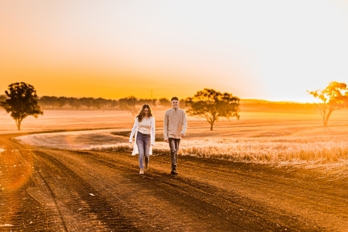 Boy and girl walking together on rural dirt road at sunset - Australian Stock Image
