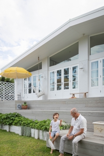 Boy and grandfather sitting together in backyard - Australian Stock Image