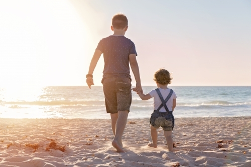Boy And Little Girl Walking Towards The Ocean At Golden Sunset - Australian Stock Image