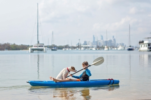 Boy at play with dog on kayak in water - Australian Stock Image