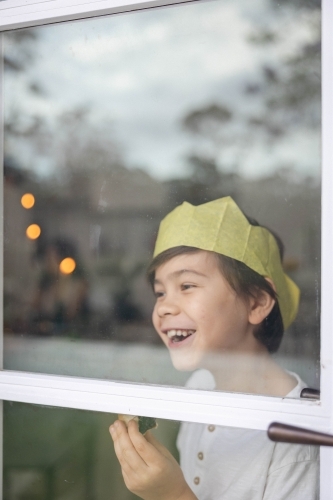 Boy at window wearing a Christmas crown and eating a mince pie - Australian Stock Image