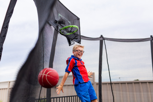 Boy bouncing on trampoline playing ball game on overcast day after school - Australian Stock Image