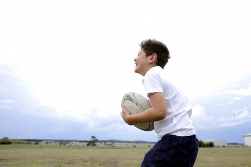 Boy catching a football in a rural paddock - Australian Stock Image