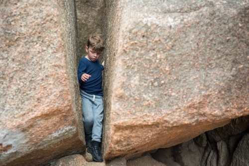Boy climbing through two boulder rocks