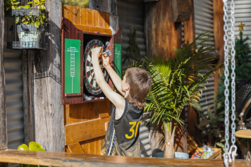 Boy collecting darts from outdoor dartboard - Australian Stock Image