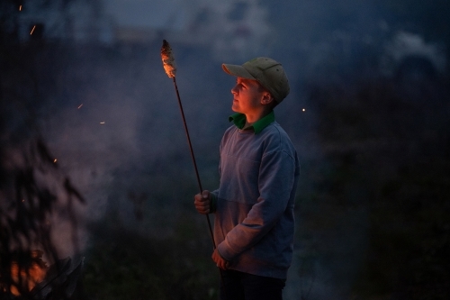 Boy cooks damper on bonfire - Australian Stock Image