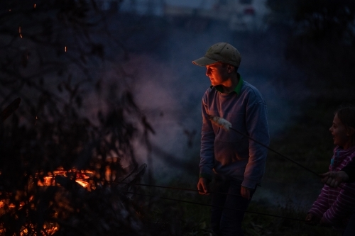 Boy cooks damper on bonfire - Australian Stock Image