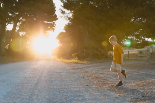 Boy crossing country dirt road at sunset - Australian Stock Image