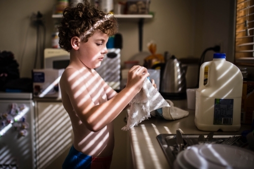 Boy doing dishes in kitchen with light from vertical blinds