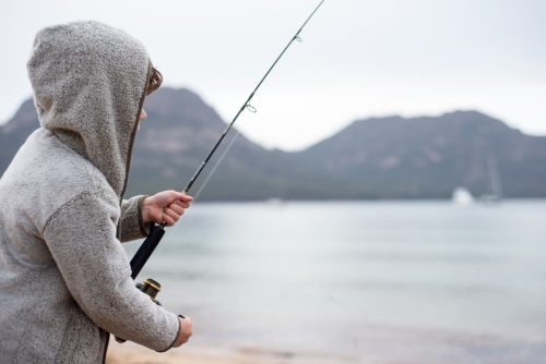 Boy fishing on a beach surrounded by mountains