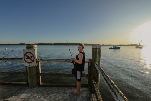Boy fishing on jetty at Iluka, NSW Australia - Australian Stock Image