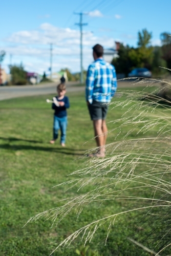 Boy flying plane with father on green grass - Australian Stock Image
