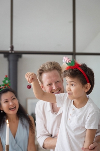 Boy holding cherry at christmas lunch with parents behind - Australian Stock Image