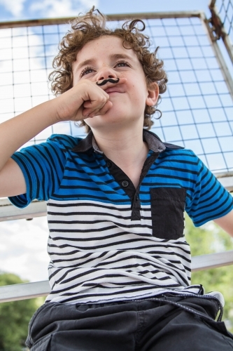 Boy holding finger with moustache tattoo under nose - Australian Stock Image