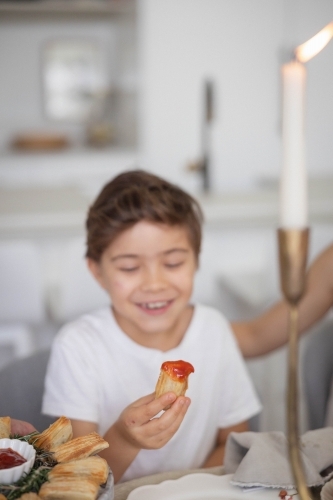 Boy holding pastry with tomato sauce at kitchen table - Australian Stock Image