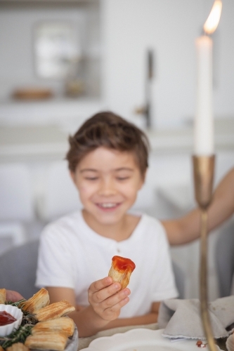 Boy holding pastry with tomato sauce at kitchen table - Australian Stock Image