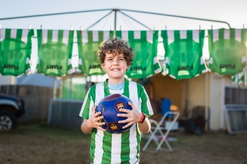 Boy holding soccer ball with team shirts hanging behind