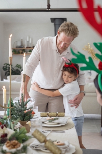 Boy hugging dad pouring water at Christmas table - Australian Stock Image