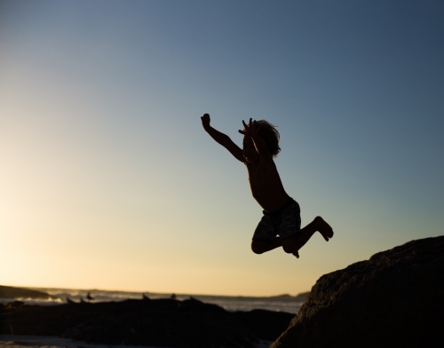 Boy jumping off a rock on the beach