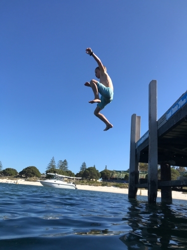 Boy jumping off jetty into river - Australian Stock Image