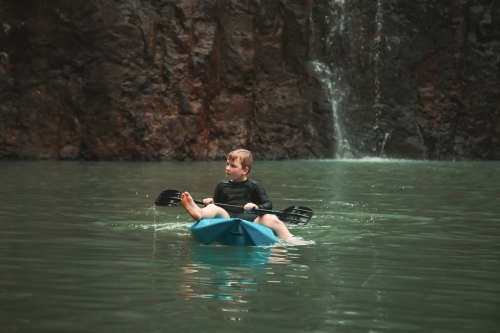 Boy kayaking with paddle in cool blue water at Cedar Creek Falls in the Whitsundays - Australian Stock Image